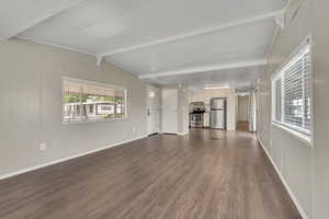 Unfurnished living room with dark wood-style flooring, lofted ceiling with beams, and a decorative wall