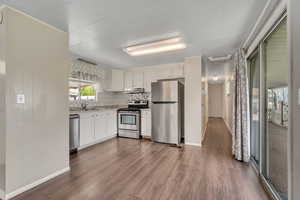 Kitchen featuring stainless steel appliances, dark wood-style floors, white cabinetry, and backsplash