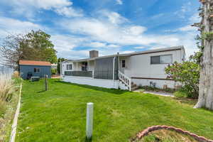 Rear view of house with a lawn, an outdoor structure, a chimney, and covered porch