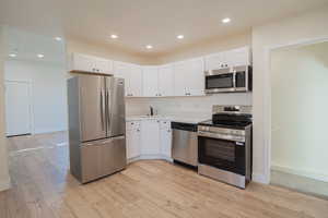 Kitchen with stainless steel appliances, white cabinetry, light wood finished floors, and recessed lighting