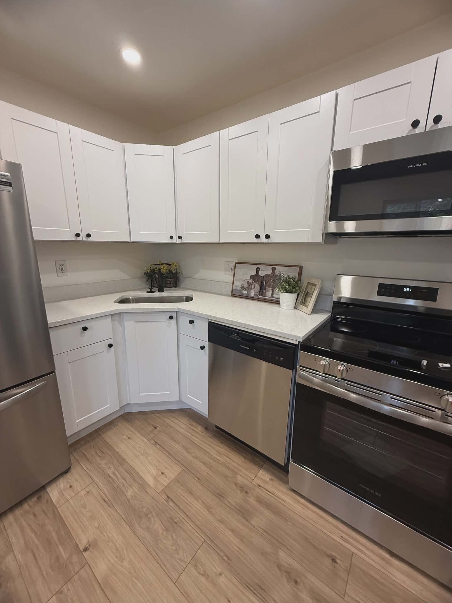 Kitchen featuring white shaker-style cabinetry, stainless steel appliances, light-toned countertops, and wood-finish flooring