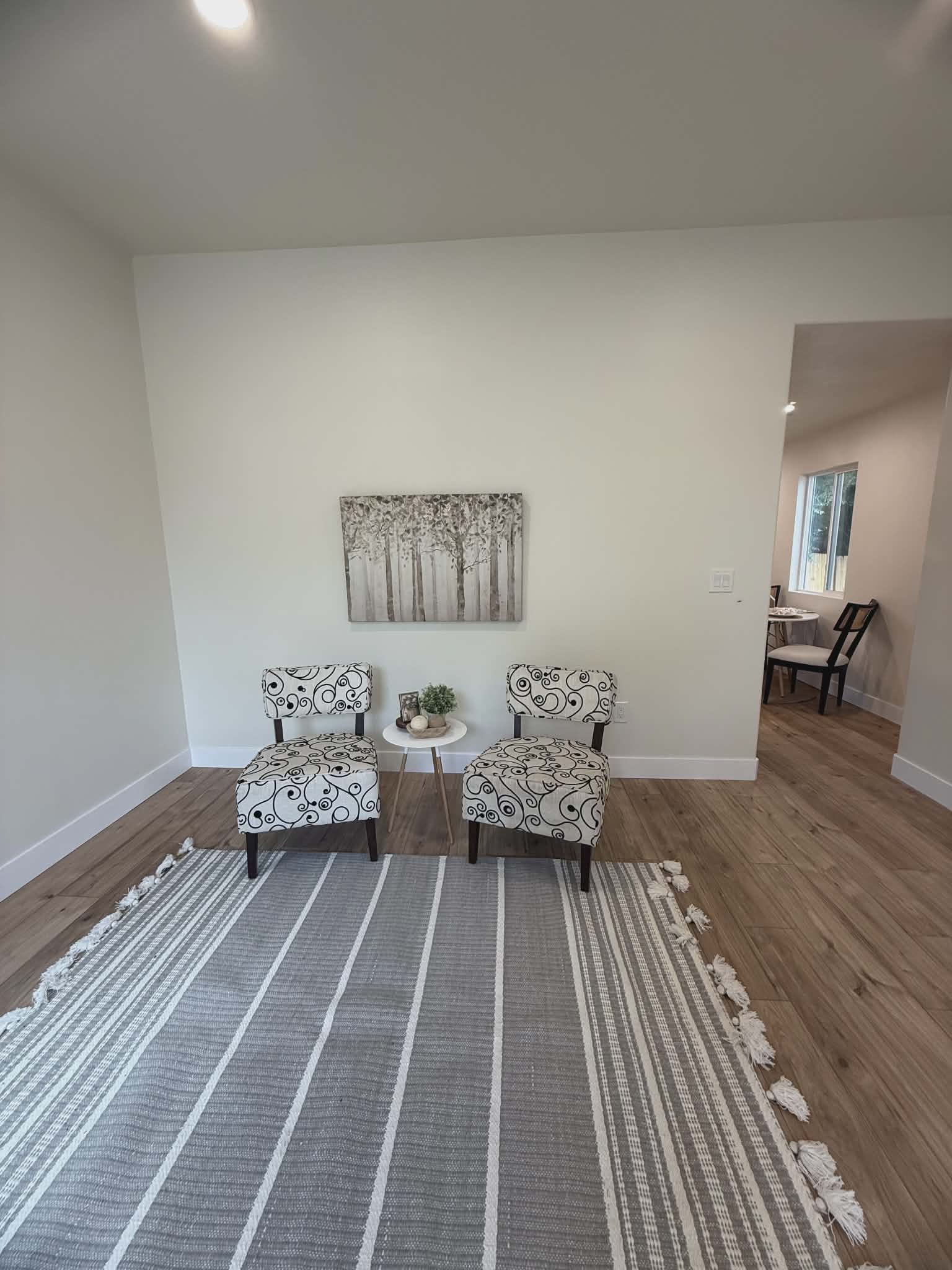 Recessed ceiling lighting illuminates a spacious room featuring light wood-finish flooring and white baseboards