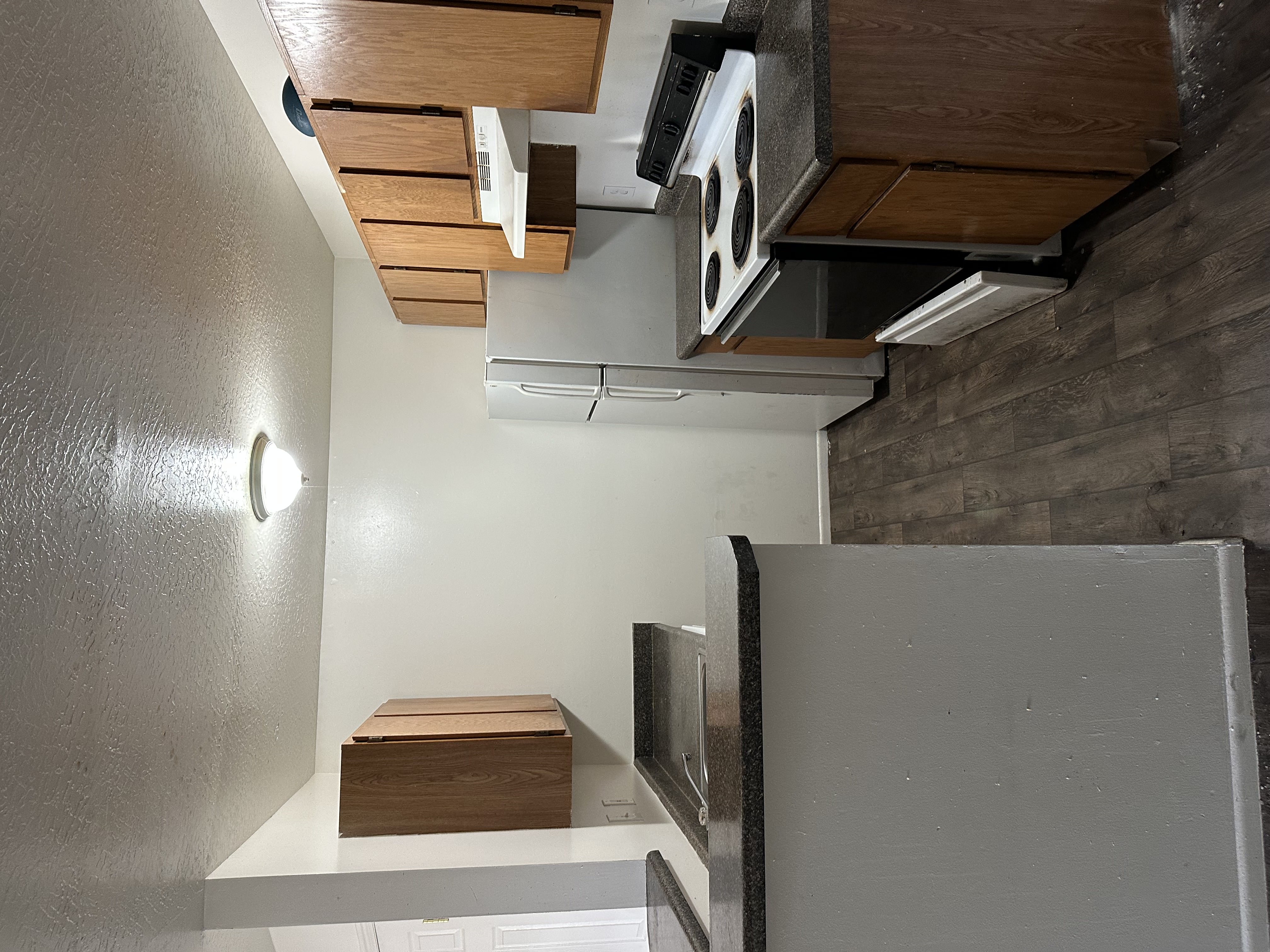 Kitchen with electric stove, dark countertops, a textured ceiling, wood finish cabinetry, and dark wood-style floors