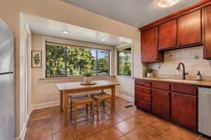 Kitchen featuring stainless steel appliances, dark tile patterned flooring, decorative backsplash, light stone countertops, and recessed lighting