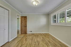 Unfurnished bedroom with light wood-style floors, crown molding, and a closet