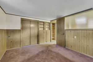 Unfurnished bedroom featuring wood walls, carpet, wainscoting, crown molding, and a closet