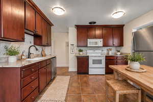 Kitchen with stainless steel appliances, light stone countertops, dark tile patterned flooring, and decorative backsplash
