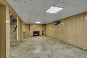 Finished below grade area with a brick fireplace, wood walls, and a drop ceiling