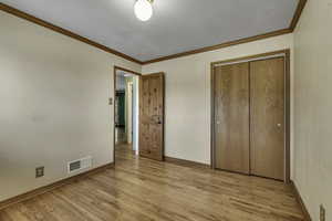 Unfurnished bedroom with crown molding, light wood-style floors, and a closet