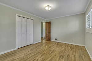Unfurnished bedroom featuring crown molding, light wood finished floors, and a closet