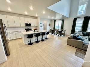 Kitchen with stainless steel appliances, open floor plan, white cabinets, a breakfast bar, and light wood-style floors