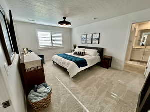 Bedroom featuring light colored carpet, a textured ceiling, and connected bathroom