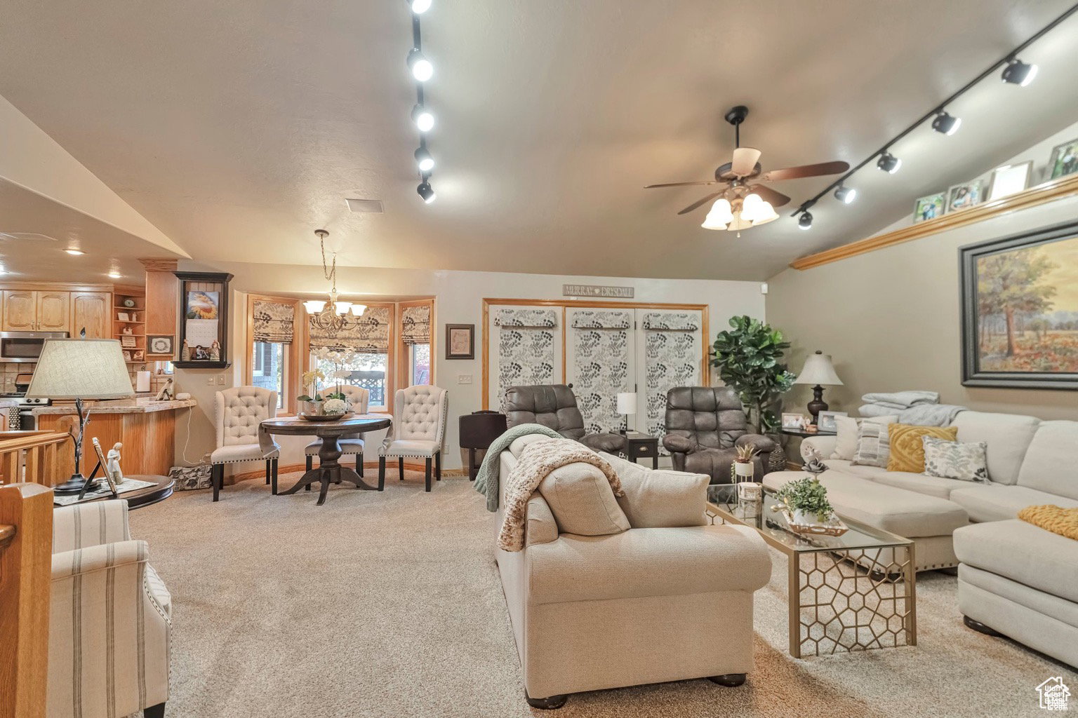 Living room with vaulted ceiling, light carpet, ceiling fan, and suspended lighting