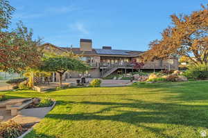 Back of house featuring a patio, roof mounted solar panels, a lawn, and a chimney