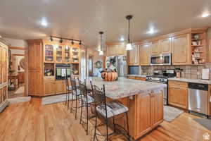 Kitchen with open shelves, a center island, a kitchen bar, stainless steel appliances, and light wood-style flooring