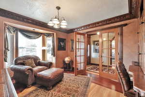 Living area with french doors, wood finished floors, a textured ceiling, and suspended lighting