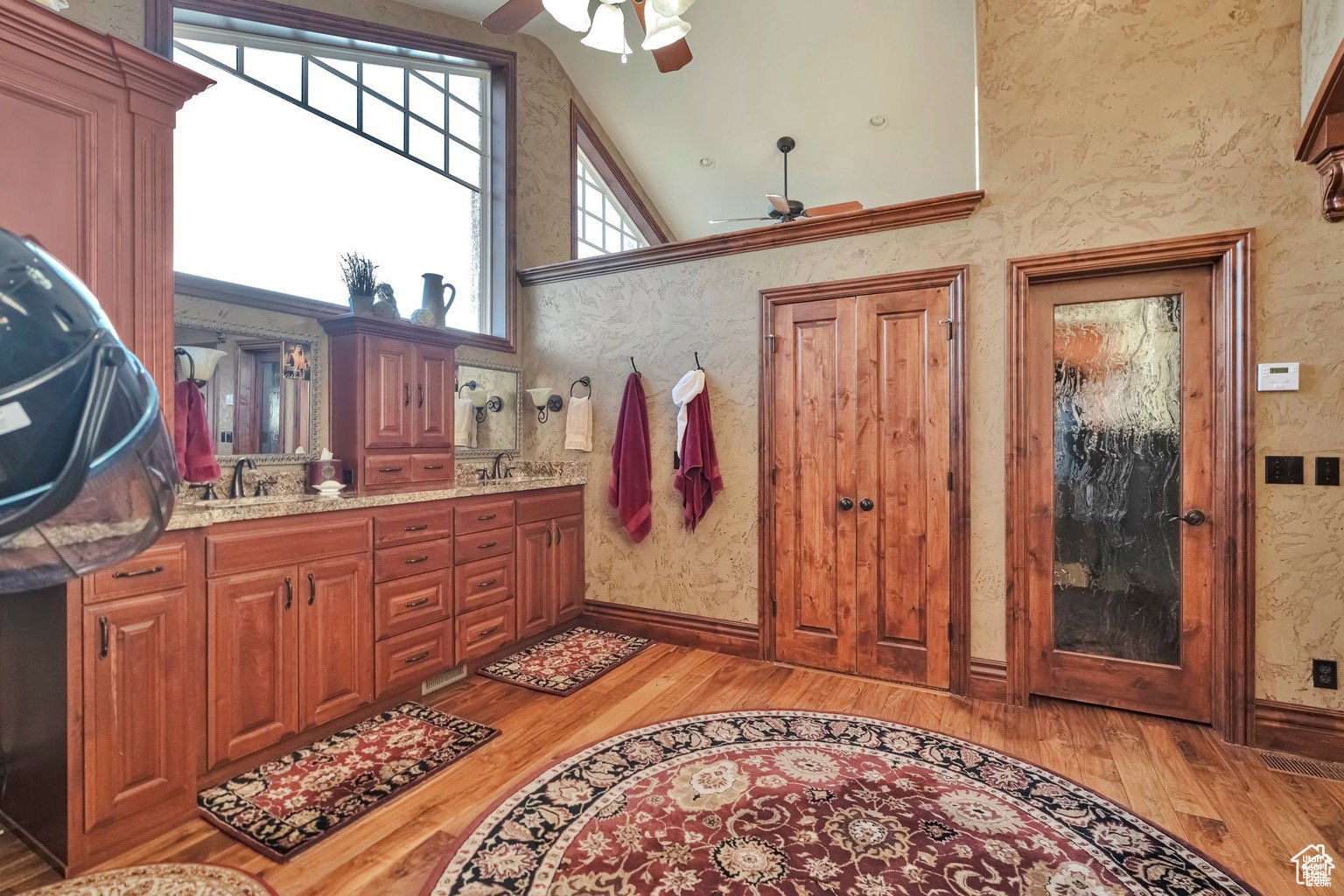 Full bath with light wood-type flooring, ceiling fan, double vanity, and vaulted ceiling