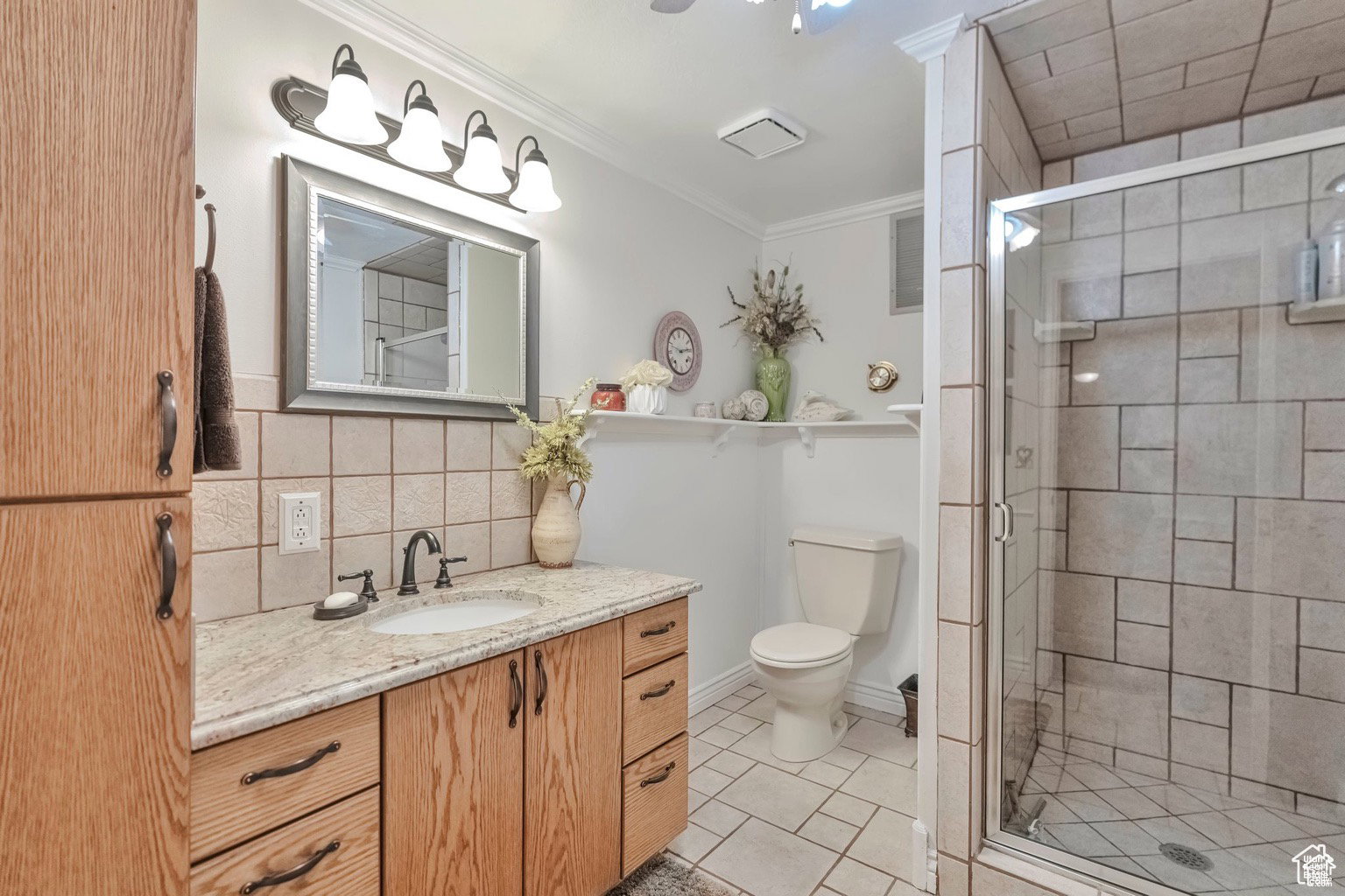 Full bath featuring vanity, a stall shower, crown molding, light tile patterned floors, and tasteful backsplash