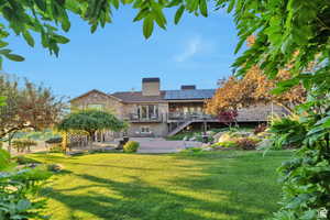 Back of house with stone siding, roof mounted solar panels, a patio area, a balcony, and a lawn