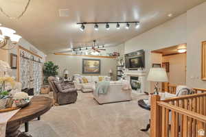 Living area featuring vaulted ceiling, ceiling fan, carpet floors, a glass covered fireplace, and hanging lights