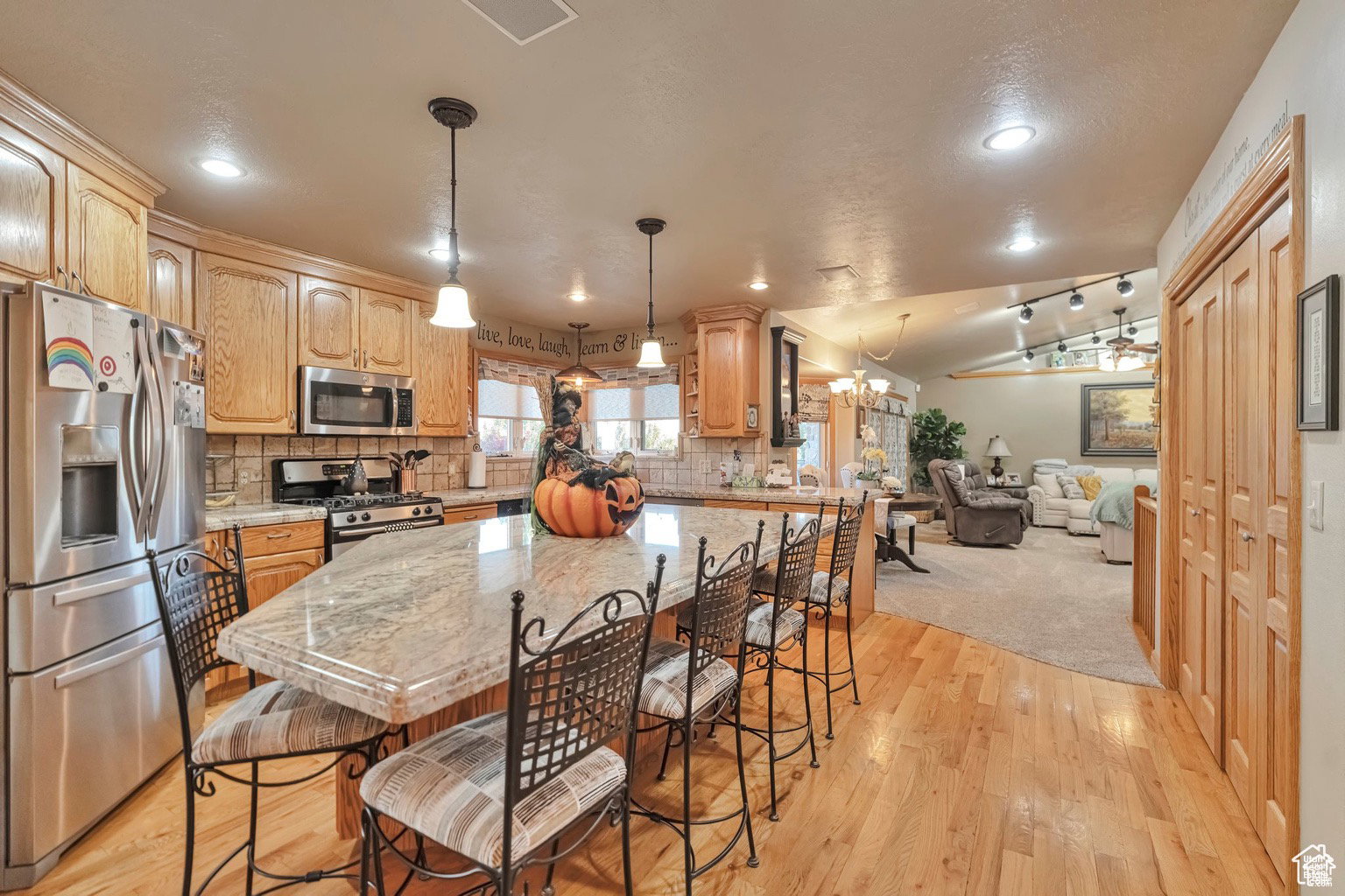 Kitchen with stainless steel appliances, a breakfast bar area, a kitchen island, light wood finished floors, and lofted ceiling