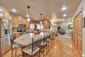 Kitchen with stainless steel appliances, a breakfast bar area, a kitchen island, light wood finished floors, and lofted ceiling