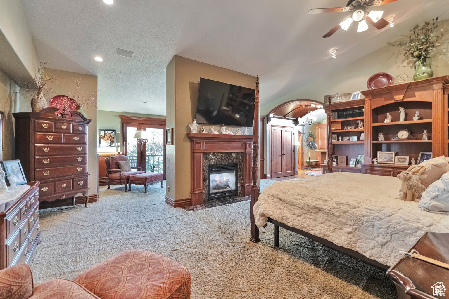 Bedroom with a fireplace, light carpet, arched walkways, a textured ceiling, and ceiling fan