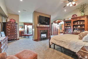Bedroom with a fireplace, light carpet, arched walkways, a textured ceiling, and ceiling fan