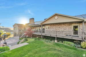 Rear view of house featuring a chimney, a yard, a wooden deck, brick siding, and solar panels