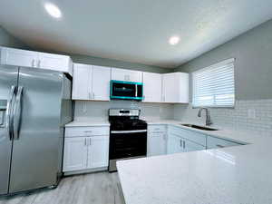 Kitchen featuring stainless steel appliances, white cabinetry, light stone counters, light wood-type flooring, and decorative backsplash