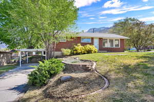 Ranch-style home featuring brick siding, a mountain view, a carport, and a front lawn