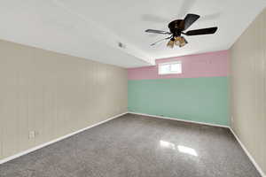 Carpeted spare room with wooden walls and ceiling fan