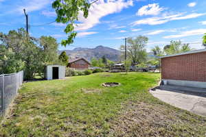 Fenced backyard featuring a storage unit, an outdoor fire pit, and a mountain view