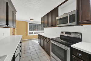 Kitchen with stainless steel appliances, dark wood finish cabinetry, light countertops, a textured ceiling, and crown molding