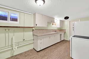 Kitchen featuring freestanding refrigerator, a textured ceiling, white cabinetry, and tile countertops