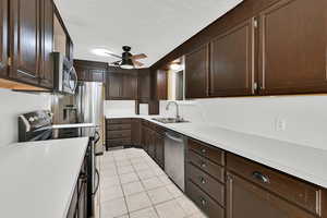 Kitchen featuring stainless steel appliances, dark wood finish cabinetry, light countertops, light tile patterned floors, and ceiling fan