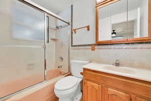 Bathroom with tile walls, vanity, shower / bath combination with glass door, and wainscoting