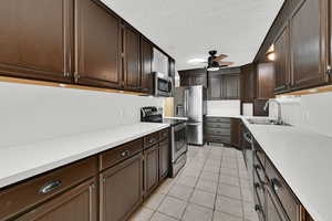 Kitchen featuring dark wood finish cabinetry, stainless steel appliances, light countertops, light tile patterned floors, and ceiling fan