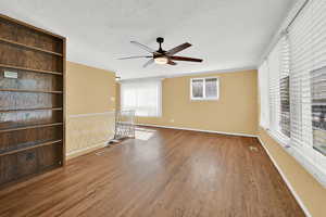 Empty room featuring a ceiling fan, dark wood-style flooring, a textured ceiling, and ornamental molding