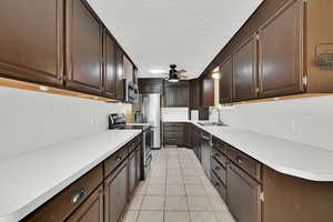 Kitchen featuring stainless steel appliances, light countertops, dark wood finish cabinets, light tile patterned floors, and a textured ceiling