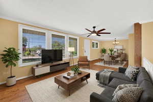 Living room featuring wood finished floors, a ceiling fan, suspended lighting, and ornamental molding