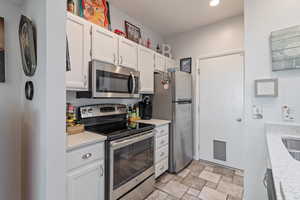 Kitchen with stainless steel appliances, white cabinetry, stone finish floors, light stone counters, and recessed lighting