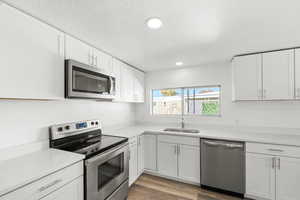 Kitchen featuring stainless steel appliances, white cabinetry, light wood finished floors, recessed lighting, and light stone counters