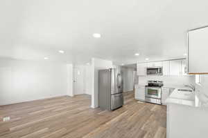 Kitchen featuring stainless steel appliances, white cabinetry, light wood finished floors, light stone countertops, and recessed lighting