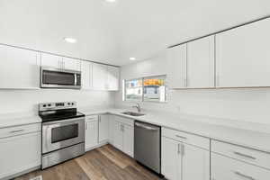 Kitchen featuring stainless steel appliances, white cabinetry, dark wood-style flooring, recessed lighting, and light stone counters