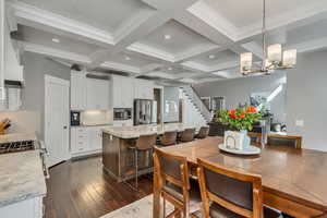 Dining room with dark wood finished floors, coffered ceiling, a chandelier, and crown molding