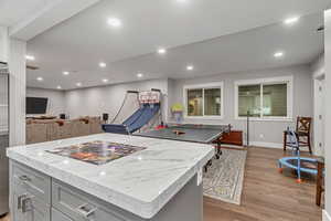 Kitchen featuring a kitchen island, gray cabinets, light wood-type flooring, light stone countertops, and open floor plan