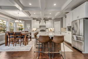 Kitchen featuring stainless steel appliances, white cabinetry, a center island with sink, light stone countertops, and a kitchen bar