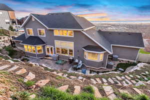 Back of property at dusk with roof with shingles, a sunroom, stucco siding, and a patio