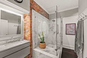 Bathroom with crown molding, a marble finish shower, vanity, and dark wood finished floors